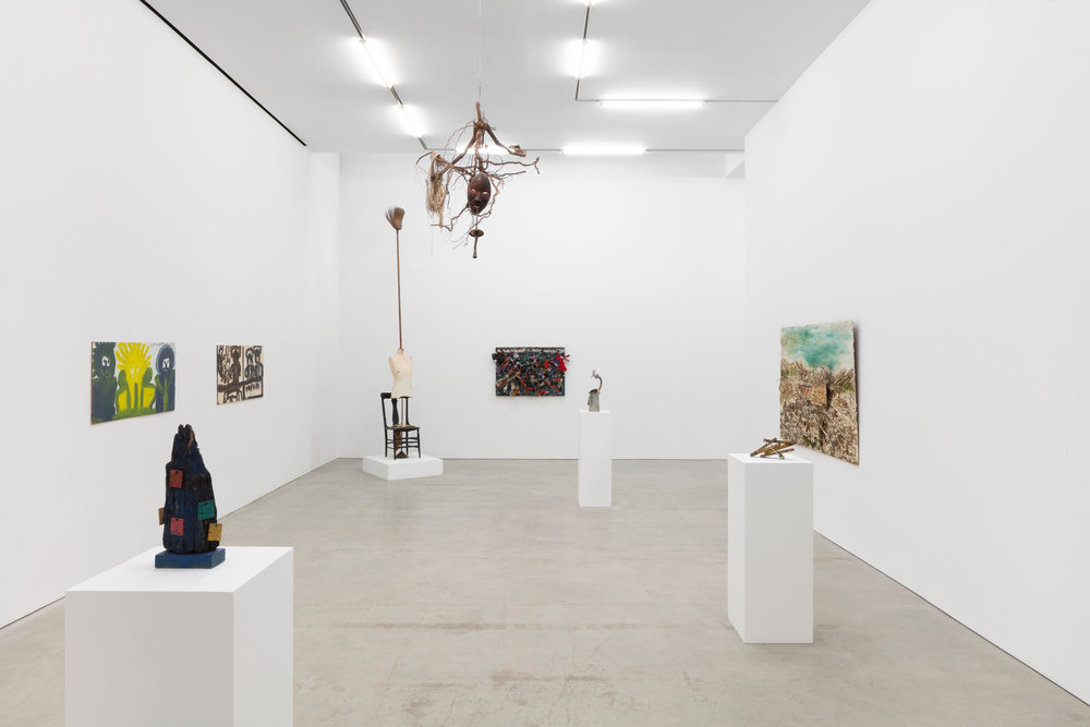An installation view of five sculptures and four paintings. One of the sculptures hangs from the gallery ceiling. 
