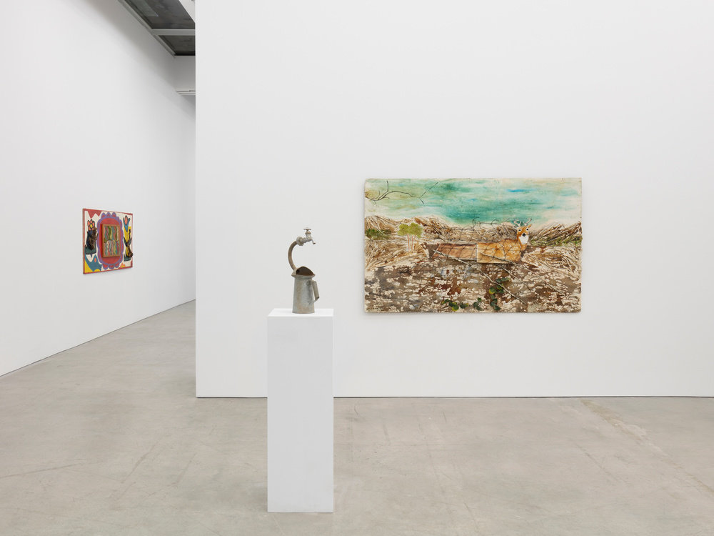 An installation view of three works. An assemblage work by Joe Light, "Driftwood Flowers", is mounted on the back left wall. Center is Lonnie Holley's sculpture, "Watering Myself the Best I Can". On the wall behind is "Traps", a painting by Ronald Lockett.