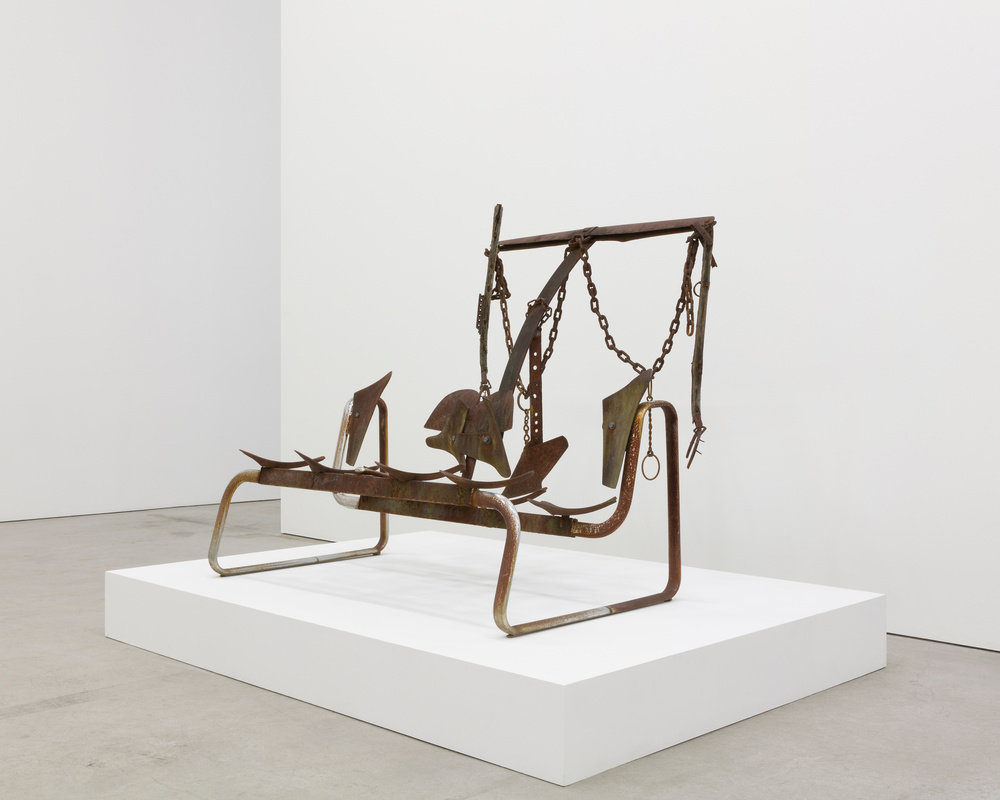 A sculpture by Joe Minter composed of antique plow parts, horseshoes, chains, a metal seat frame, and found metal.