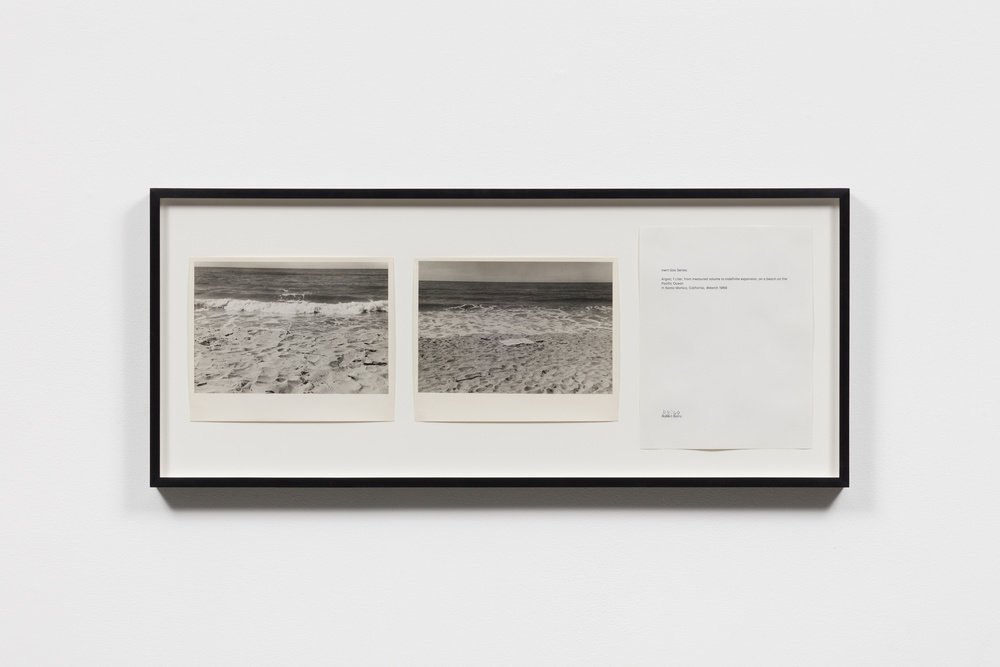 Two black and white photographs of the beach beside a white piece of paper with text, all hung in a black frame, by Robert Barry. 