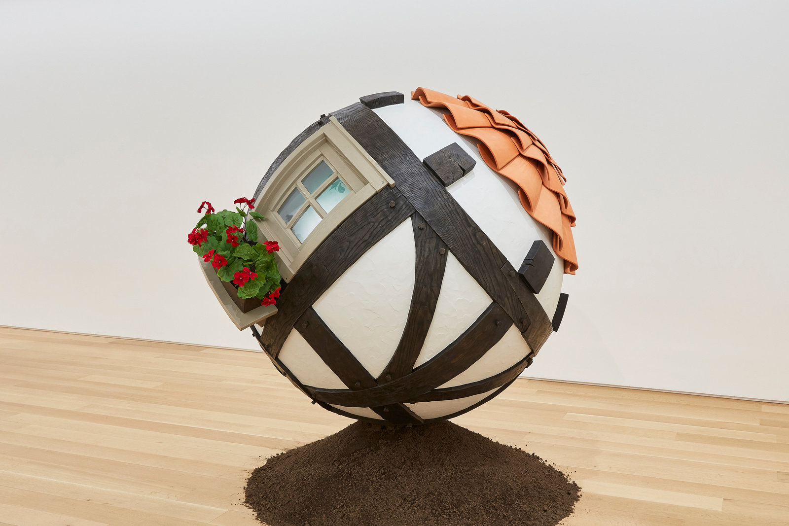 A spherical sculpture that resembles a home that sits on top of a mound of dirt by Lars Fisk. 