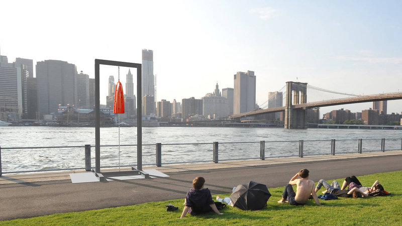 Two figures face the Manhattan skyline across the Hudson River. One of Davina Semo's bells is installed on the path along the waterfront, hanging from an armature that allows people to get close and ring it. 